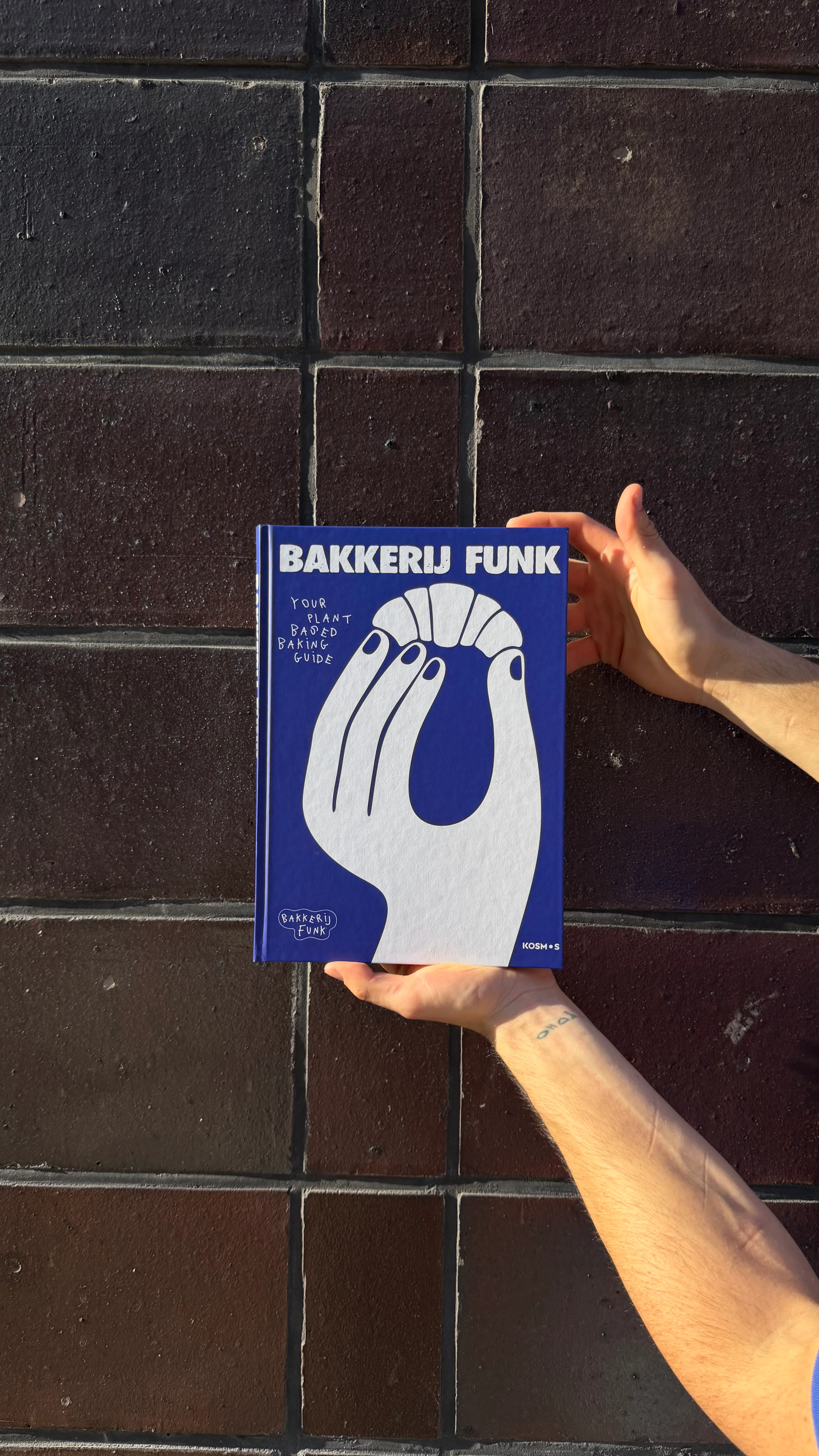 A hand holding up the Bakkerij FUNK plantbased baking guide, the FUNK bakboek