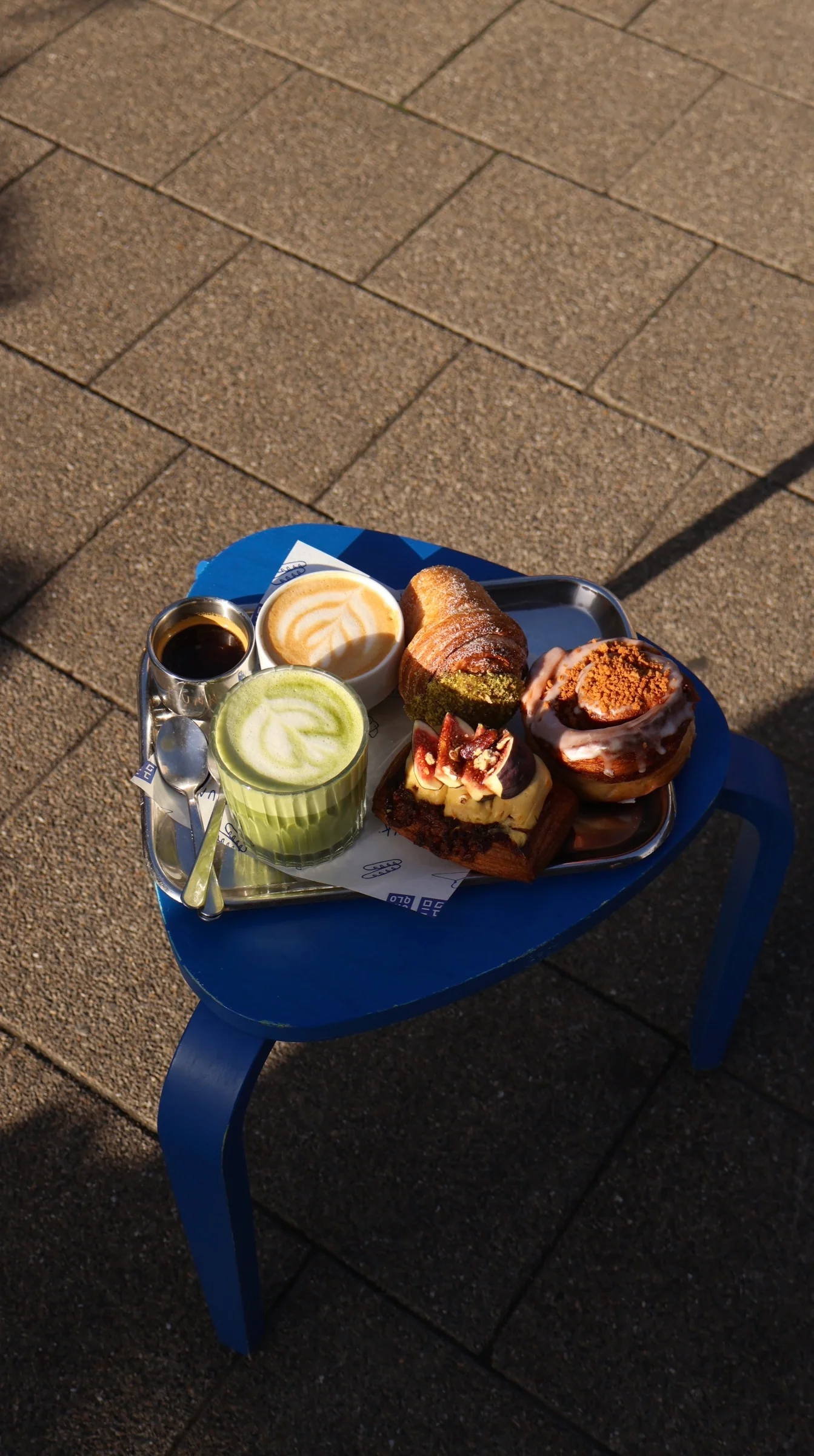 A tray of plantbased pastries and a matcha latte on a blue caf&eacute; table in the Amsterdam sun
